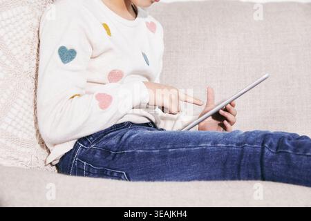 Una donna si siede su un divano, usando un tablet per navigare attraverso un'interfaccia digitale. Foto Stock