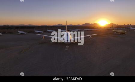 Tucson, Stati Uniti - 30 novembre 2025: Veduta aerea di un vasto disteso campo di aviazione, dove i giganti dormienti riposano sotto l'arancione e il viola infuocati gl Foto Stock