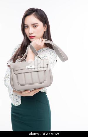 Una giovane donna asiatica regge una borsa in pelle beige, guardando direttamente la fotocamera con un'espressione neutra. Foto Stock
