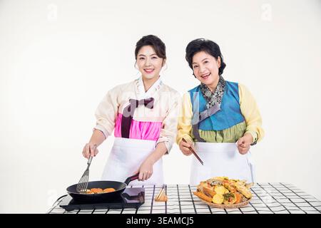 Due donne in hanbok tradizionali coreani cucinano il cibo in una cucina moderna. Foto Stock