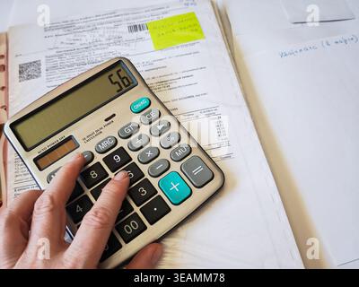Kirov, Russia - 18 marzo 2026: Person calcola le spese mensili con una calcolatrice mentre è circondata da ricevute e importanti documenti finanziari Foto Stock