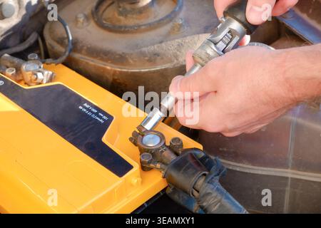 La mano del meccanico sta tirando su una vecchia batteria di un'auto per la sostituzione. Un uomo stringe con una chiave per il fissaggio di una batteria nuova, installando la p di ricambio Foto Stock