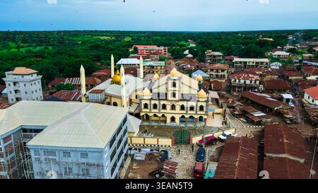 Vista aerea di un'importante moschea con cupola dorata e minareti, annidata tra fitti edifici dal tetto rosso e alberi verdi, Igbaja, Nigeria. Foto Stock