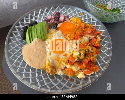 Piatto della colazione con uova soleggiate, avocado, verdure, olive e salsa su piatto di vetro. Foto mobile Foto Stock