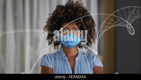 Donna in piedi che indossa una camicetta a pieghe, maschera blu e occhiali trasparenti in clinica, mascherina con archi punteggiati. Ritratto, studio, calma, softfocus, capelli curlisci, profe Foto Stock