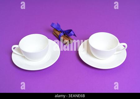Due tazze bianche vuote con bastoncini alla cannella su sfondo viola Foto Stock