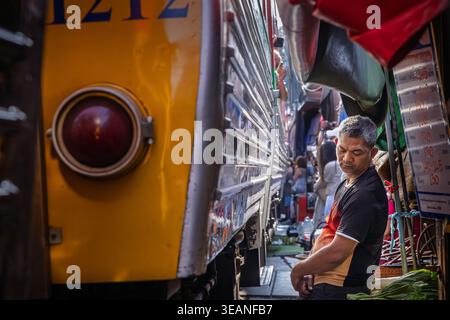 Il venditore si trova accanto a un treno di passaggio al mercato ferroviario di Maeklong a Mae Klong, nella provincia di Samut Songkhram, Thailandia Foto Stock