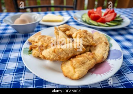 Petulla, impasto fritto dorato su un piatto bianco sopra una tovaglia a scacchi blu e bianca Foto Stock
