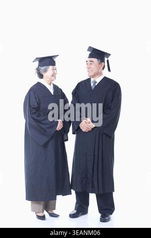 Una donna e un uomo, entrambi con abiti e berretti da laurea, stanno insieme, sorridono e guardano l'un l'altro. Foto Stock