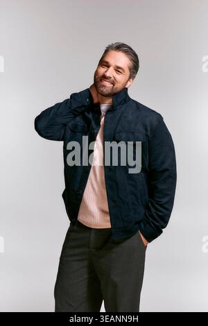 Un bell'uomo sorride con sicurezza, indossando strati alla moda che ne mettono in risalto lo stile. Foto Stock