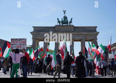 Berlino, Germania - 23 aprile 2026: Durante la sua visita, i contro-manifestanti hanno un segnale critico contro Reza Pahlavi di fronte alla porta di Brandeburgo. Foto Stock