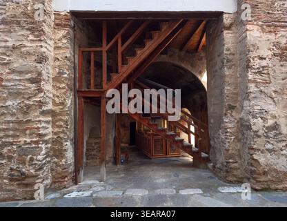 Tradizionale scalinata in legno all'interno del Monastero di Bachkovo con pareti in pietra e mattoni in muratura, archi e dettagli del cortile in un ambiente monastico storico. Foto Stock
