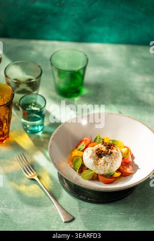 Insalata burrata caprese con pomodori cimellati colorati, basilico fresco e condimento speziato servito su un piatto rustico Foto Stock