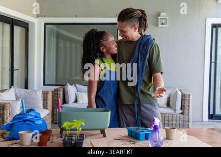 Coppia afroamericana che si occupa di piantine sul patio coperto al tavolo da vaso con piantatrice. Giardinaggio, piante, veranda, all'aperto, insieme, accogliente, n Foto Stock