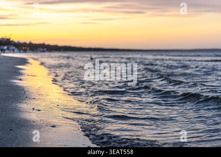 Piccole onde sulla spiaggia di sabbia la sera. Luce dorata del tramonto sull'acqua. Foto Stock