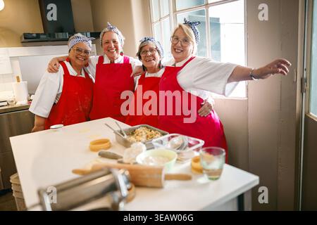Un gruppo di quattro donne anziane gioiose che posa e ridono in un laboratorio di cucina Foto Stock