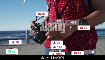 Reflex digitale regolabile, donna con la parte superiore a pois rossa e jeans che incorniciano la passerella sul mare con cuori fluttuanti Foto Stock