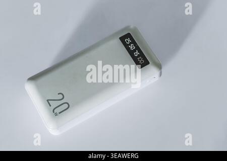 Una vista dall'alto verso il basso di un elegante power Bank portatile bianco appoggiato su una superficie bianca semplice. Il dispositivo è dotato di un testo di 20 W. Foto Stock