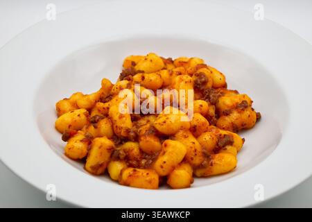 Un piatto bianco ripieno di gnocchi di patate deliziosi e una ricca salsa bolognese di carne isolata su fondo bianco. Foto Stock