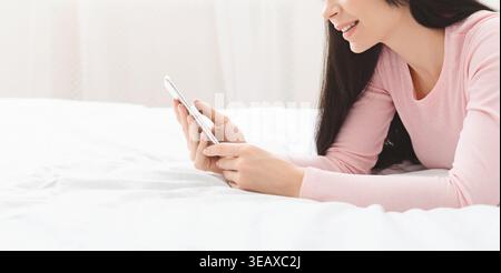 Giovane donna che si diverte a divertirsi mentre usa lo smartphone in un'accogliente camera da letto Foto Stock