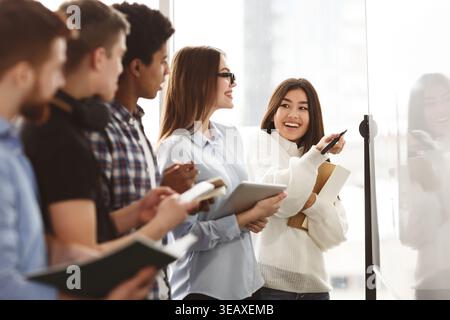 Gruppo di studenti che collaborano durante una presentazione in un'aula luminosa Foto Stock