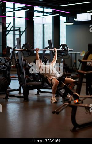 Ripresa verticale di un giovane adulto che esegue una pressa per panchina inclinata in palestra, costruendo forza e disciplina fitness. Adatto per programmi di allenamento, marketing sportivo, verticale Foto Stock