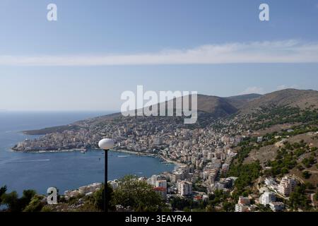Ampia vista panoramica della città di Saranda, annidata tra il Mar Ionio e le colline ondulate sotto un cielo azzurro limpido in Albania Foto Stock