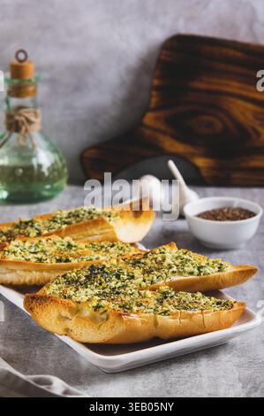 Baguette al forno con burro, aglio e aneto su un piatto con vista verticale sul tavolo Foto Stock