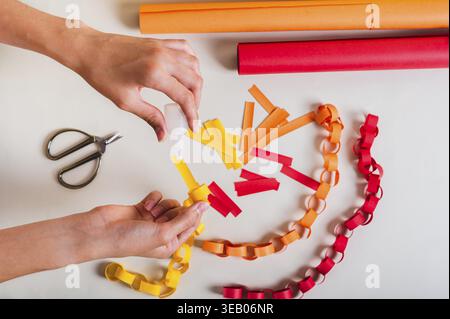 Le mani di una ragazza versano la colla su una striscia di carta per ottenere la vista dall'alto della catena di carta Foto Stock