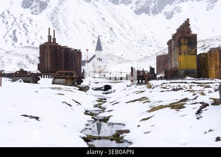 Stazione baleniera abbandonata con vasche e macchinari arrugginiti, chiesa in legno bianco sullo sfondo, nevicate, Grytviken, Georgia del Sud Foto Stock