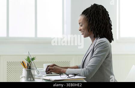 Donna impegnata a lavorare su un notebook in un moderno spazio ufficio con streaming di luce naturale Foto Stock