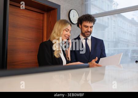 Il receptionist e il manager esaminano insieme i documenti alla reception Foto Stock