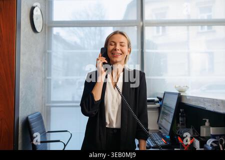 La receptionist è felice di rispondere al telefono al banco della reception dell'hotel Foto Stock