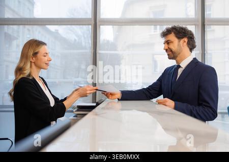 L'elegante receptionist dell'hotel consegna la tessera chiave agli ospiti d'affari presso la moderna lobby del ricevimento Foto Stock