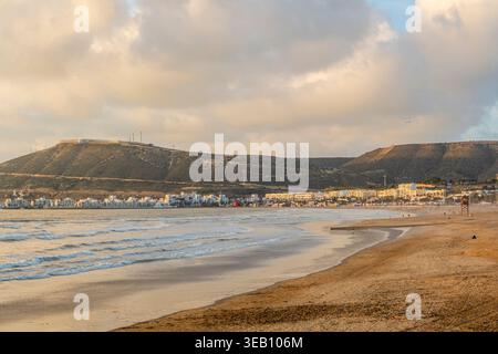 Spiaggia con sabbia, mare e cielo blu. Montagne sullo sfondo. Cielo con nuvole limpide e luce del tardo pomeriggio. Marocco, spiaggia di Agadir Foto Stock