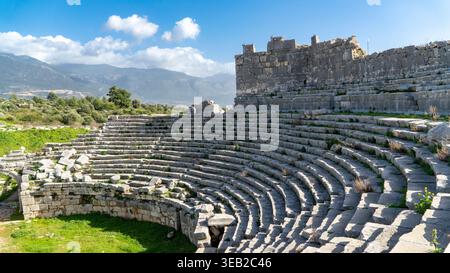 Antiche rovine romane del teatro Xanthos in Licia, Mugla, Turchia. Posti a sedere semicircolari in pietra che si affacciano su un paesaggio di montagna Foto Stock