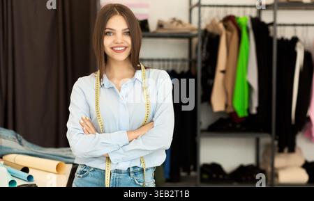 Tailor si trova in uno studio di moda, tenendo in mano il nastro di misurazione e sorridendo Foto Stock