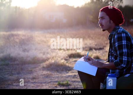 Uomo che scrive su un taccuino pensando alla creatività al tramonto Foto Stock