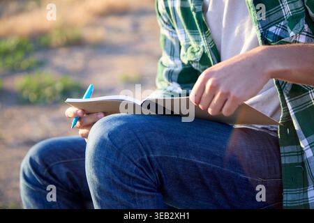 Persona che scrive su un notebook all'aperto, trova ispirazione Foto Stock