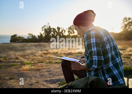 Giovane uomo che scrive su un notebook all'aperto al tramonto Foto Stock