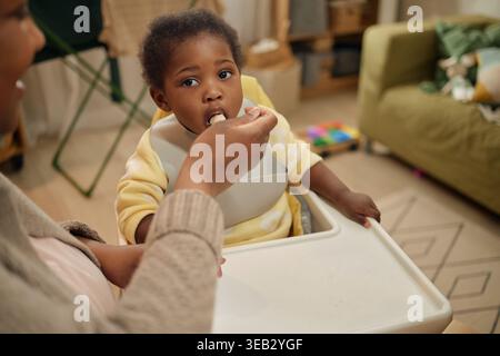 Bimbo nero che mangia mentre la mamma dà da mangiare a casa con budget limitato Foto Stock