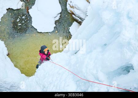 Arrampicatrice su ghiaccio che sale alla cascata ghiacciata con la corda Foto Stock