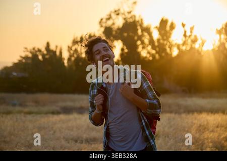 Giovane che ama la musica facendo trekking al tramonto dell'ora d'oro Foto Stock