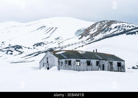 Vista di un edificio in legno abbandonato all'Isola di Deception con montagne coperte di neve e un cielo coperto dall'Antartide. Foto Stock