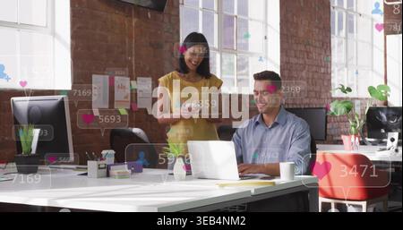 Colleghi di lavoro che esaminano il laptop in ufficio, con camicia blu e parte superiore gialla, mostrando icone di reazione Foto Stock