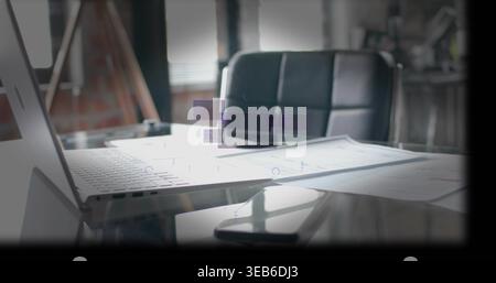 Visualizzazione di un laptop aperto color argento e grandi planimetrie su una scrivania in vetro in ufficio, con riflesso nero del telefono Foto Stock
