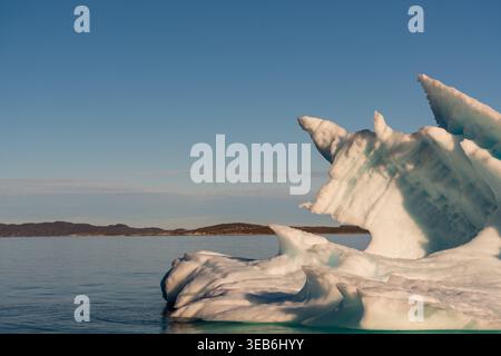 Vista di un grande iceberg con picchi frastagliati che fluttuano nelle calme acque blu di un fiordo con lontane colline rocciose sotto un cielo limpido a Nuuk, Sermer Foto Stock