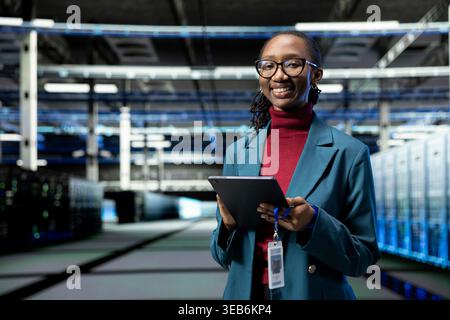 Ritratto di un ingegnere donna felice nel data center che utilizza un tablet per monitorare le metriche dei sistemi di perforazione. Donna sorridente in una server farm che utilizza applicazioni per dispositivi per migliorare l'efficacia operativa dell'infrastruttura Foto Stock
