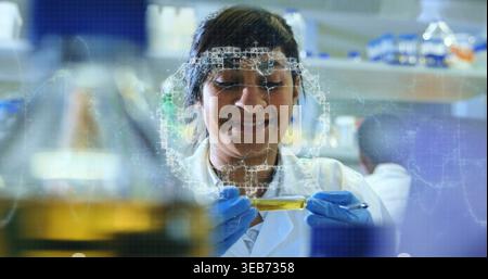 Esaminatrice scienziata che tiene in mano la provetta di prova in laboratorio, indossando un camice da laboratorio bianco e guanti blu in nitrile Foto Stock