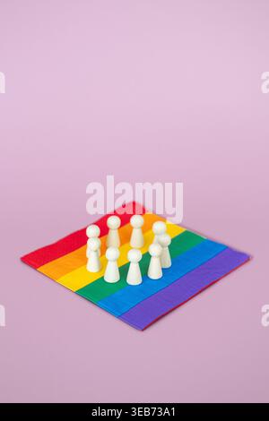 Un gruppo di statuette di legno si erge in cerchio sulla bandiera arcobaleno con sfondo rosa. DEI Diversity, Equity, and Inclusion policy Implementation Foto Stock
